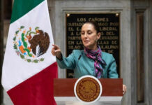 Person speaking at podium with Mexican flag nearby