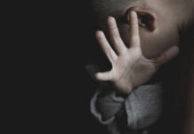 Child covering face with hand in dim light