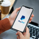 Person holding smartphone with PayPal logo displayed