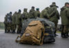 Military backpacks on ground, soldiers standing in background.