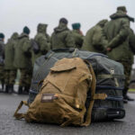 Military backpacks on ground, soldiers standing in background.