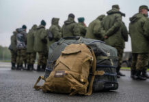 Military backpacks on ground, soldiers standing in background.
