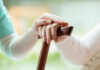 Hands on a wooden cane with a supportive hand on top