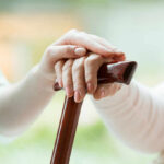 Hands on a wooden cane with a supportive hand on top