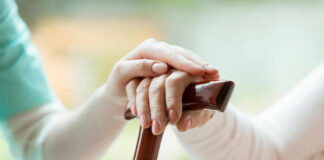 Hands on a wooden cane with a supportive hand on top