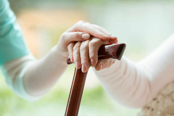 senior-holding-hands-on-walking-cane740531920jpg Hands on a wooden cane with a supportive hand on top