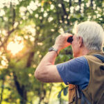 Senior man using binoculars to observe nature during sunset