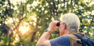 Senior man using binoculars to observe nature during sunset