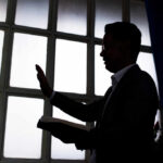 Silhouette of a person holding a book and raising a hand