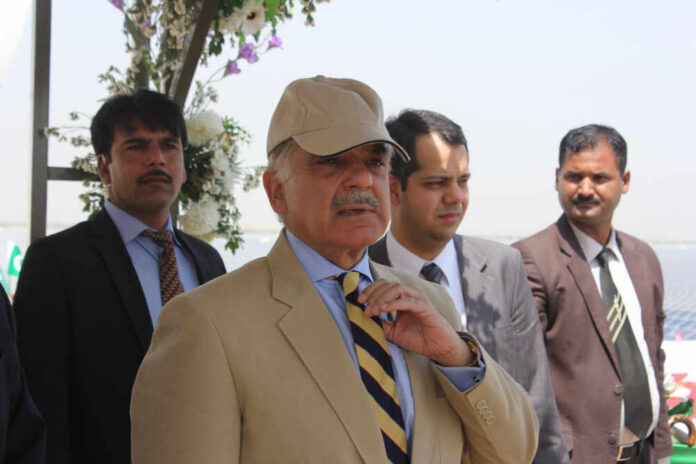 A group of men in formal attire at an outdoor event, with one man wearing a cap