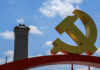 Large yellow communist symbol in front of a monument against a blue sky