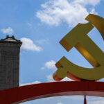 Large yellow communist symbol in front of a monument against a blue sky