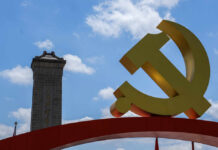 Large yellow communist symbol in front of a monument against a blue sky