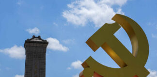Large yellow communist symbol in front of a monument against a blue sky