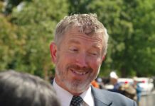A smiling man in a suit engaging in conversation outdoors