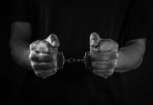 Fugitive Strangler Exploits Europe’s Justice Loophole Hands holding handcuffs in a black and white image