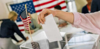 Hand placing ballot in box with American flag nearby
