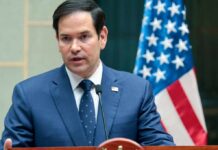 TikTok Smear on Rubio Crashes Into CAMERA FACTS A man in a blue suit speaking into a microphone with an American flag in the background