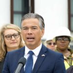 Man in a navy suit speaking at a microphone with people standing behind