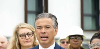 Man in a navy suit speaking at a microphone with people standing behind
