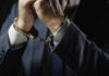 Mob Enforcer Back In Cuffs — Town Shaken Businessperson in suit with hands cuffed together