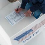 Trump’s $350B Military Bill Comes With a Voter ID Fight Person filling out a ballot at voting booth.