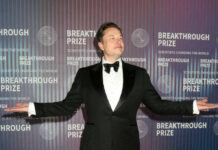 man in a tuxedo posing with arms outstretched at an awards event
