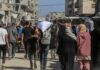 UN Warns Iran War Could Push 45 Million More Into Hunger Crowd walking through a dusty street between damaged buildings