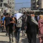 UN Warns Iran War Could Push 45 Million More Into Hunger Crowd walking through a dusty street between damaged buildings