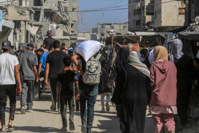 Crowd walking through a dusty street between damaged buildings