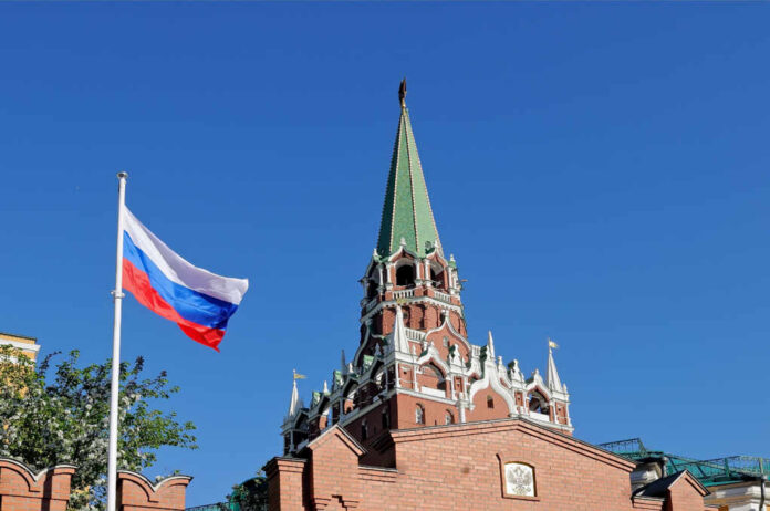 National,Flag,Of,Russia,Against,Troitskaya,Tower,Of,The,Moscow Russian flag and Kremlin tower against a clear blue sky