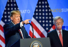 Two men at a press conference with U.S. flags behind them