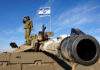 Israel Pounds Tyre — Justified Or Blunder? Soldier saluting from atop a tank with an Israeli flag in the background
