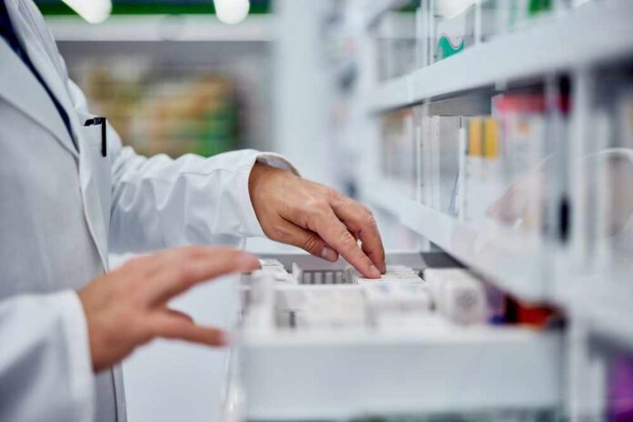 Male,Pharmacist,Choosing,A,Medicine,From,The,Drawer,,Side,View. Pharmacist organizing medication on a shelf