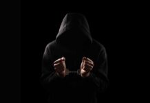 Convicted Teen’s Haunting Line Caught On Tape A hooded figure with hands in handcuffs against a dark background