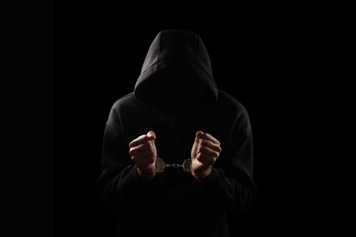Silhouette,Of,Handcuffed,Male,In,Hoodie,,Dangerous,Criminal,Punished,By A hooded figure with hands in handcuffs against a dark background