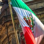 Person speaking at podium with Mexican flag nearby