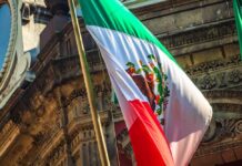 Person speaking at podium with Mexican flag nearby