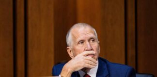 A politician sitting at a desk with a thoughtful expression during a hearing