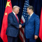 Two political leaders shaking hands in front of national flags