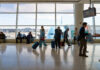 Passengers in an airport terminal with luggage and an airplane visible outside
