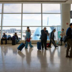 Passengers in an airport terminal with luggage and an airplane visible outside