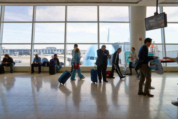 New,York,-,April,06,,2016:,Inside,Of,Jfk,Airport. Passengers in an airport terminal with luggage and an airplane visible outside