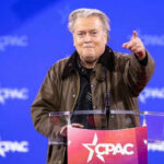 Bannon Blasts Mullin Over Bovino Comment Person speaking at CPAC conference blue background