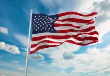 Patriotism Branded Dangerous — Backlash Erupts American flag waving on a flagpole against a blue sky with clouds