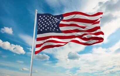 1874470474 American flag waving on a flagpole against a blue sky with clouds