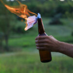 hand holding a glass bottle with a burning rag