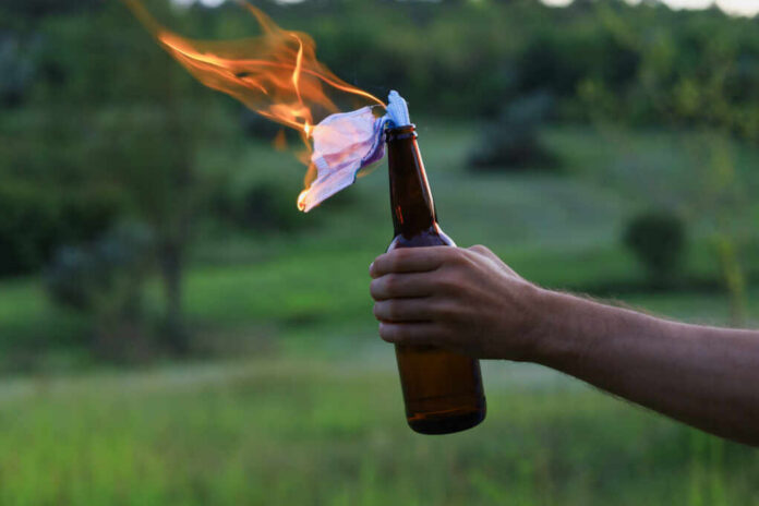 Burning,Molotov,Cocktail,On,Blurred,Background,Of,Hand,Of,White hand holding a glass bottle with a burning rag
