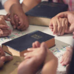 Nigeria’s Blindfold: Killers Walk Free People holding hands with Bibles on table
