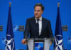 Man speaking at podium with NATO flags behind him